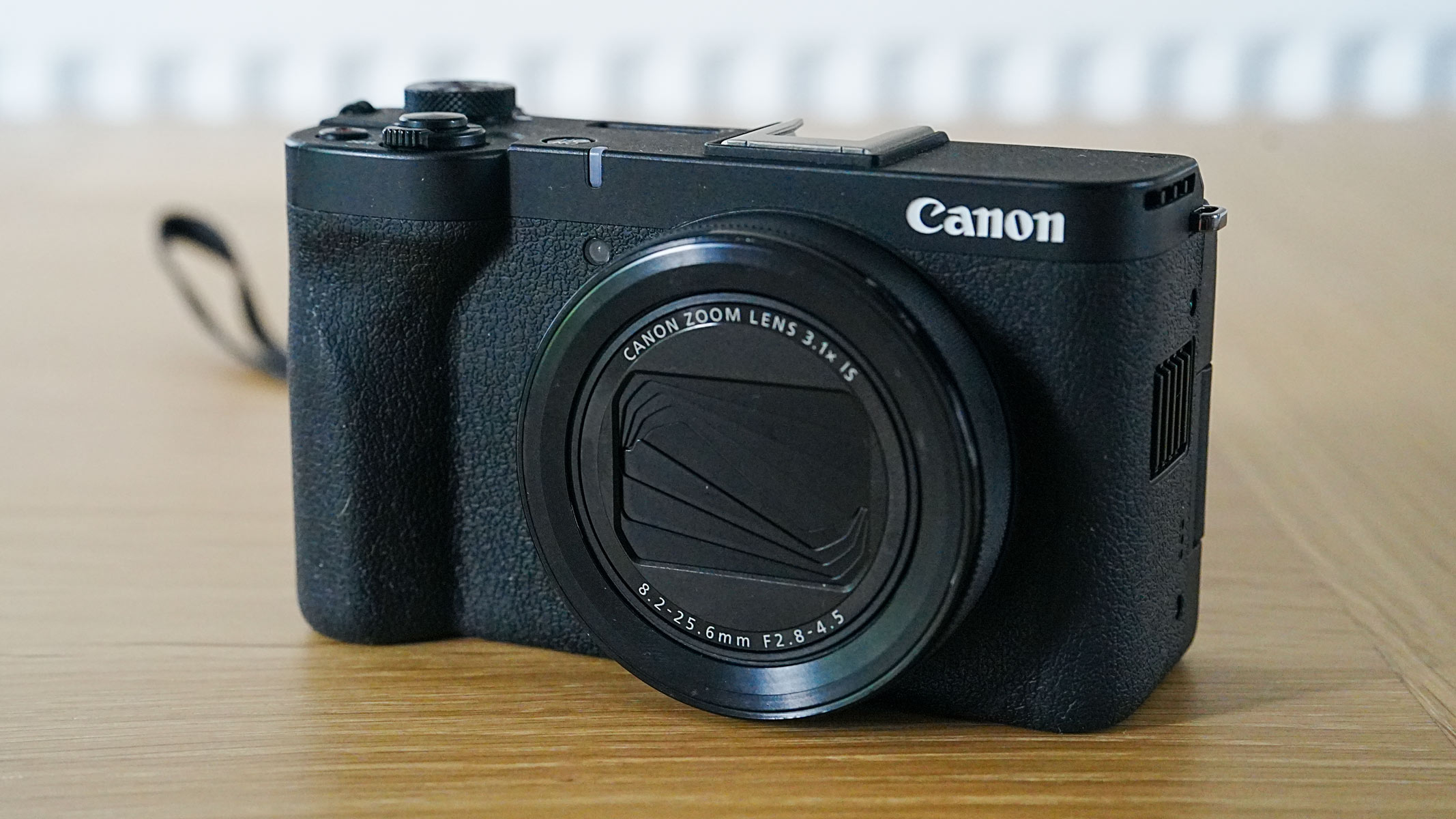 A Canon Powershot V1 with shutter closed on a wooden table.
