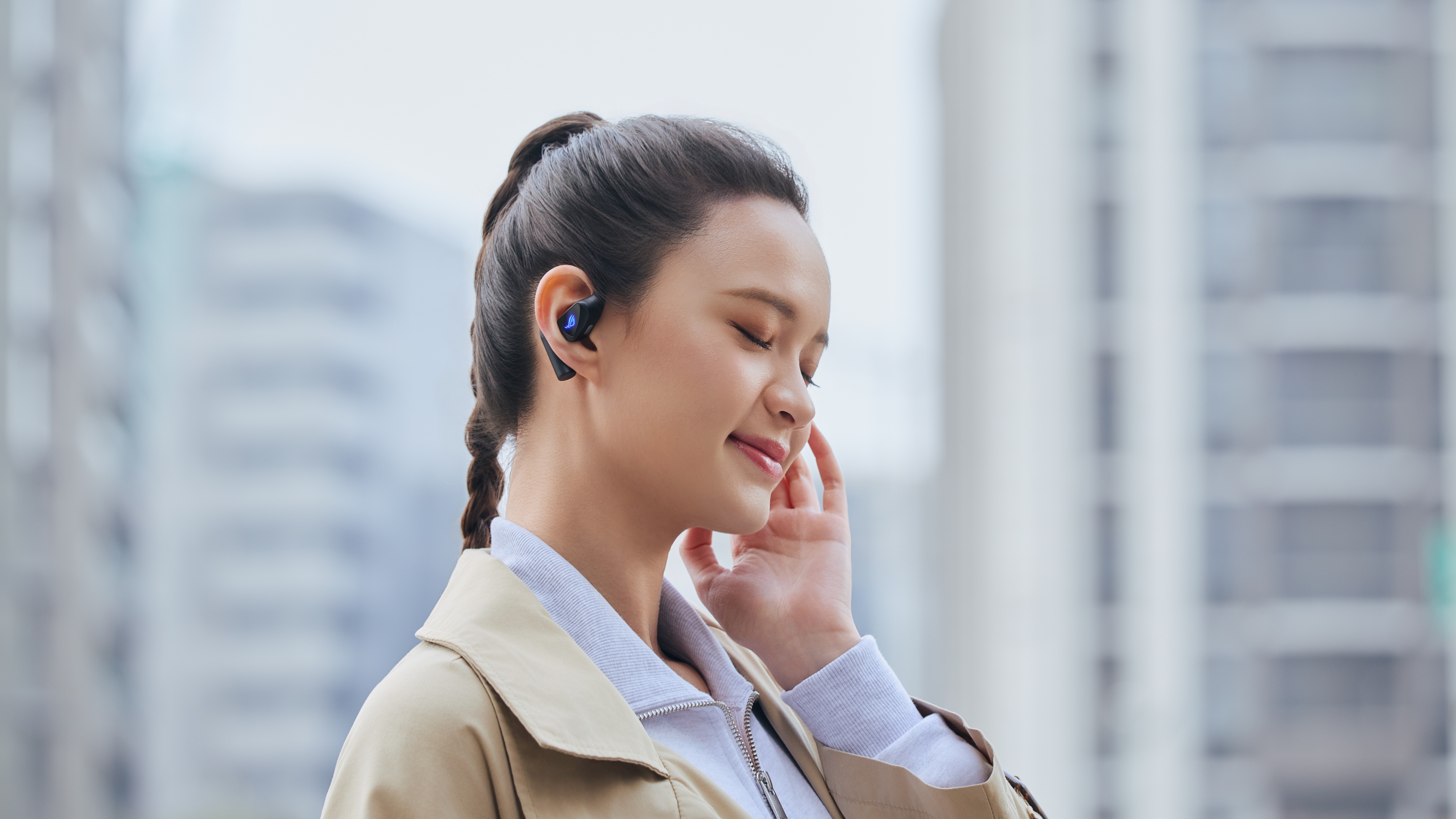 A woman using the new Asus ROG Cetra Open wireless open-ear earbuds to listen to music in a city.