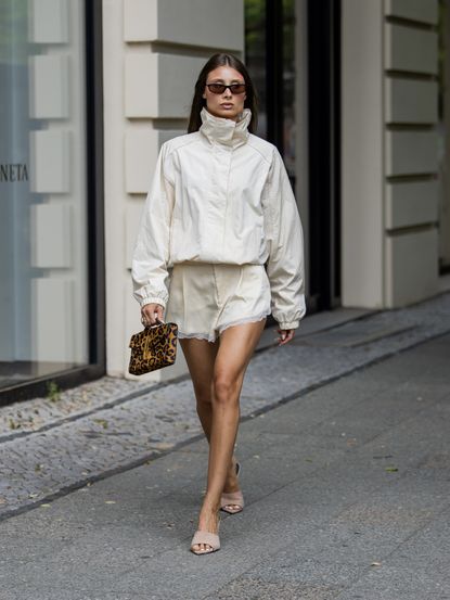 stylish woman wearing a cream funnel neck jacket and cream silk shorts