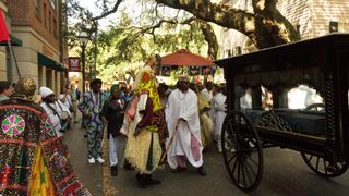 The procession of Ancestors to their original resting place in the reinterment ceremony; individuals enclosed in reinforced boxes wrapped in indigo cloth were placed in a horse-drawn hearse and taken to the site, accompanied by an Egungun Masquerade, spiritual leaders, and members of the community. 