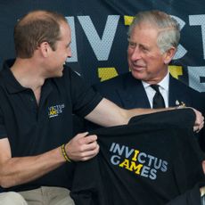 Prince William holding a black Invictus Games shirt up to King Charles