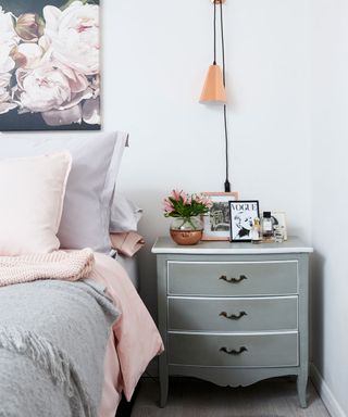 Grey bedside table with drawers next to bed and wall with floral painting