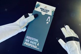 photo of a pamphlet reading "bring taste to space" held by a hand wearing a black-and-white astronaut glove