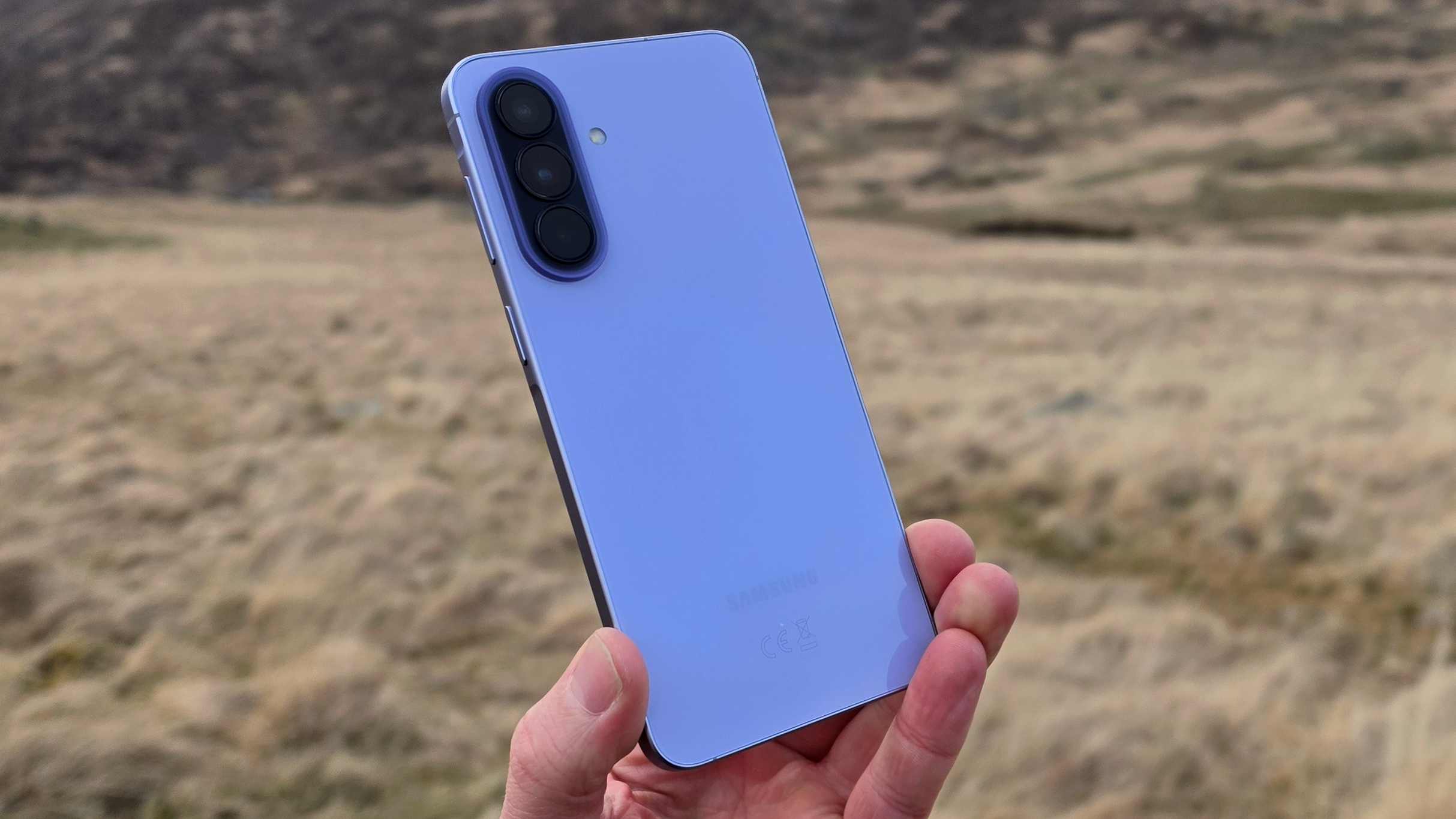 The Samsung Galaxy A57 being held over a field, showing its rear.