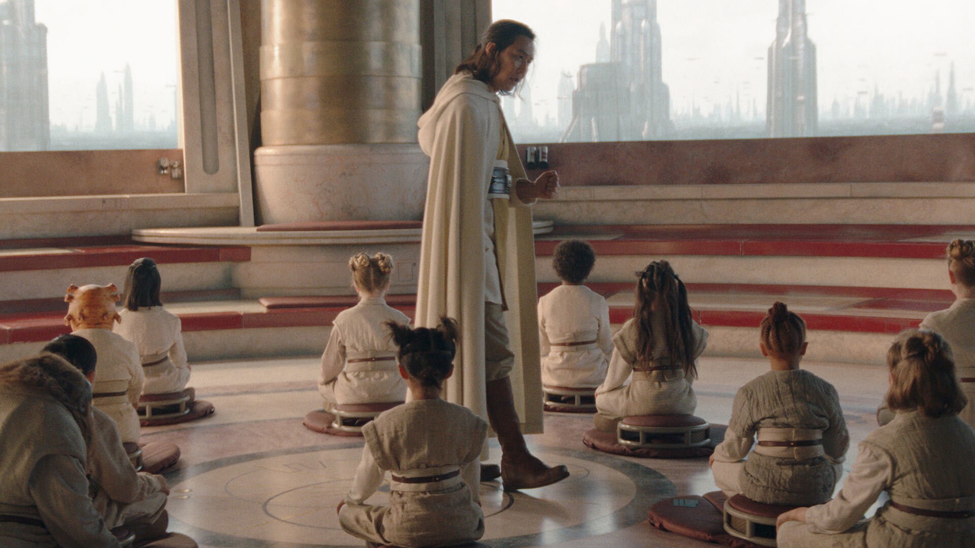 A man in a long white robe walks amid a floor of little kids