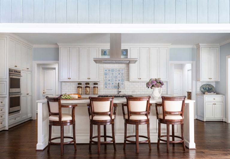 kitchen with pale blue walls and paneling with white cabinets and upholstered dark wood bar stools