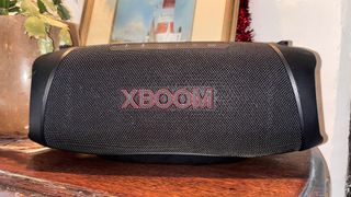 LG XBoom Go XG8T wireless speaker on wooden table in front of plant pot and picture frame