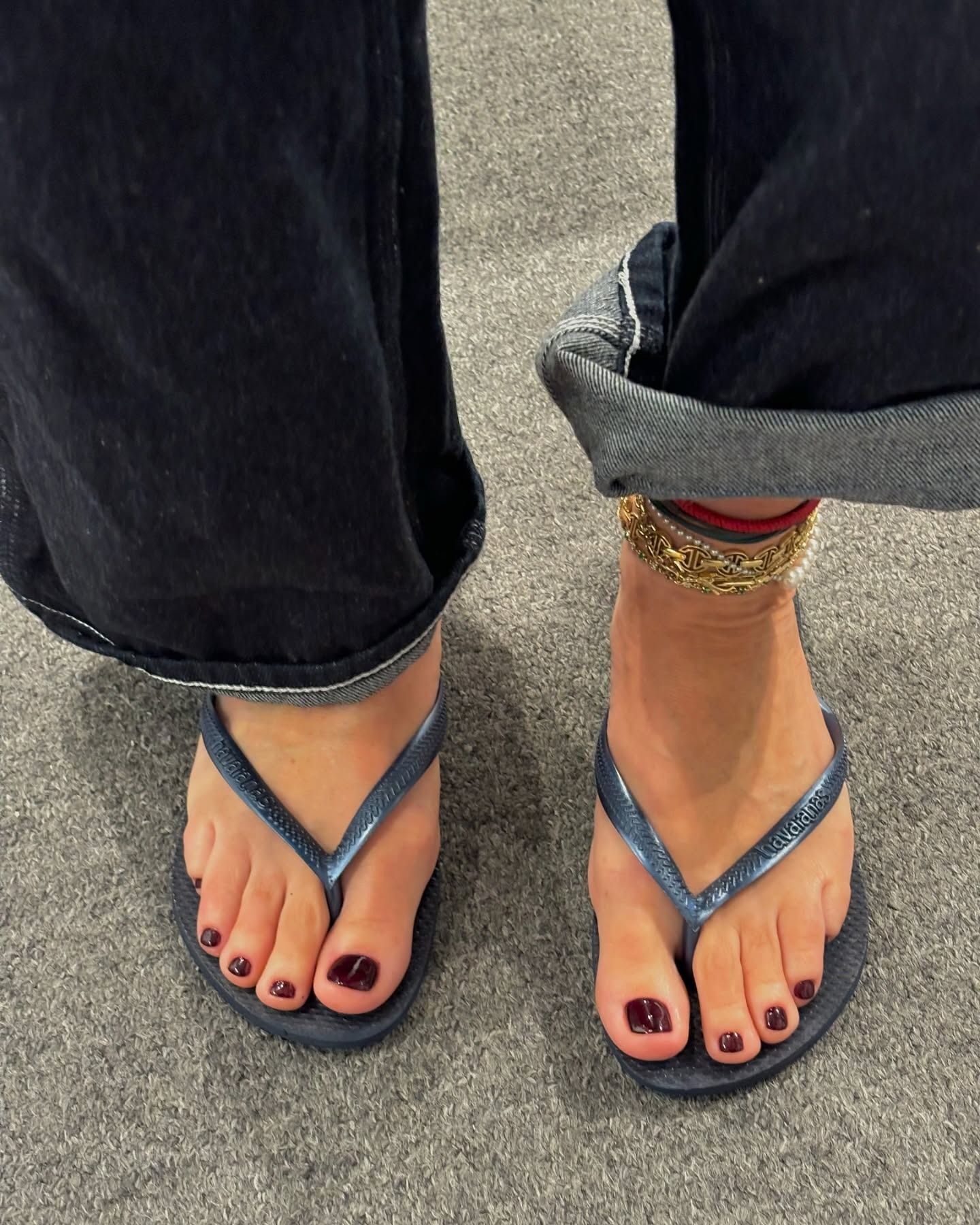 A close up of feet wearing grey flip flops and the toes painted with a dark red cherry pedicure