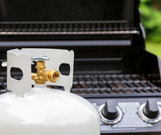 A white propane tank in front of a gas grill
