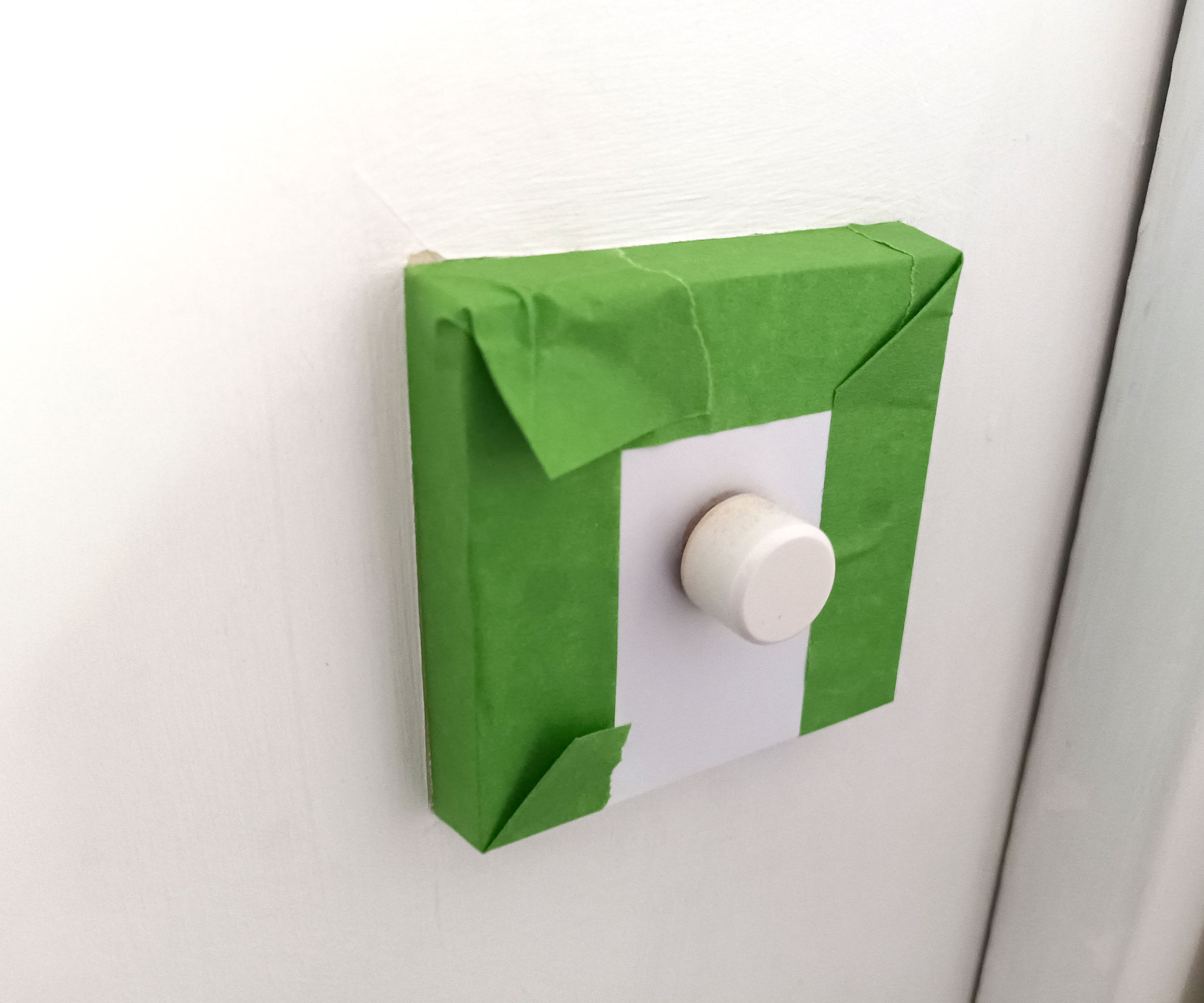 Green Frog Tape around white dimmer switch on white wall