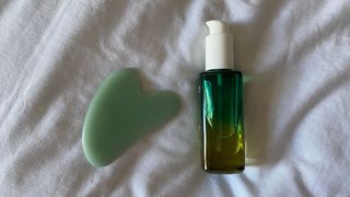 a gua sha tool and a facial oil on a white sheet background