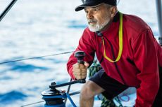 Confident skipper holding handle on winch of genoa sail on sailboat.