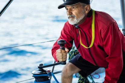 Confident skipper holding handle on winch of genoa sail on sailboat.
