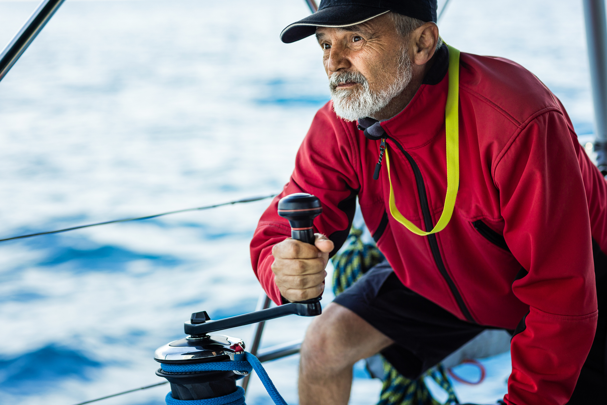 Confident skipper holding handle on winch of genoa sail on sailboat.