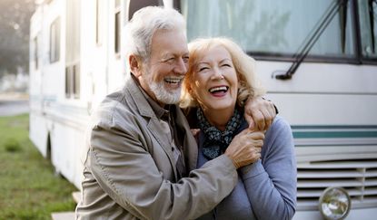 A mature couple stands near their RV.