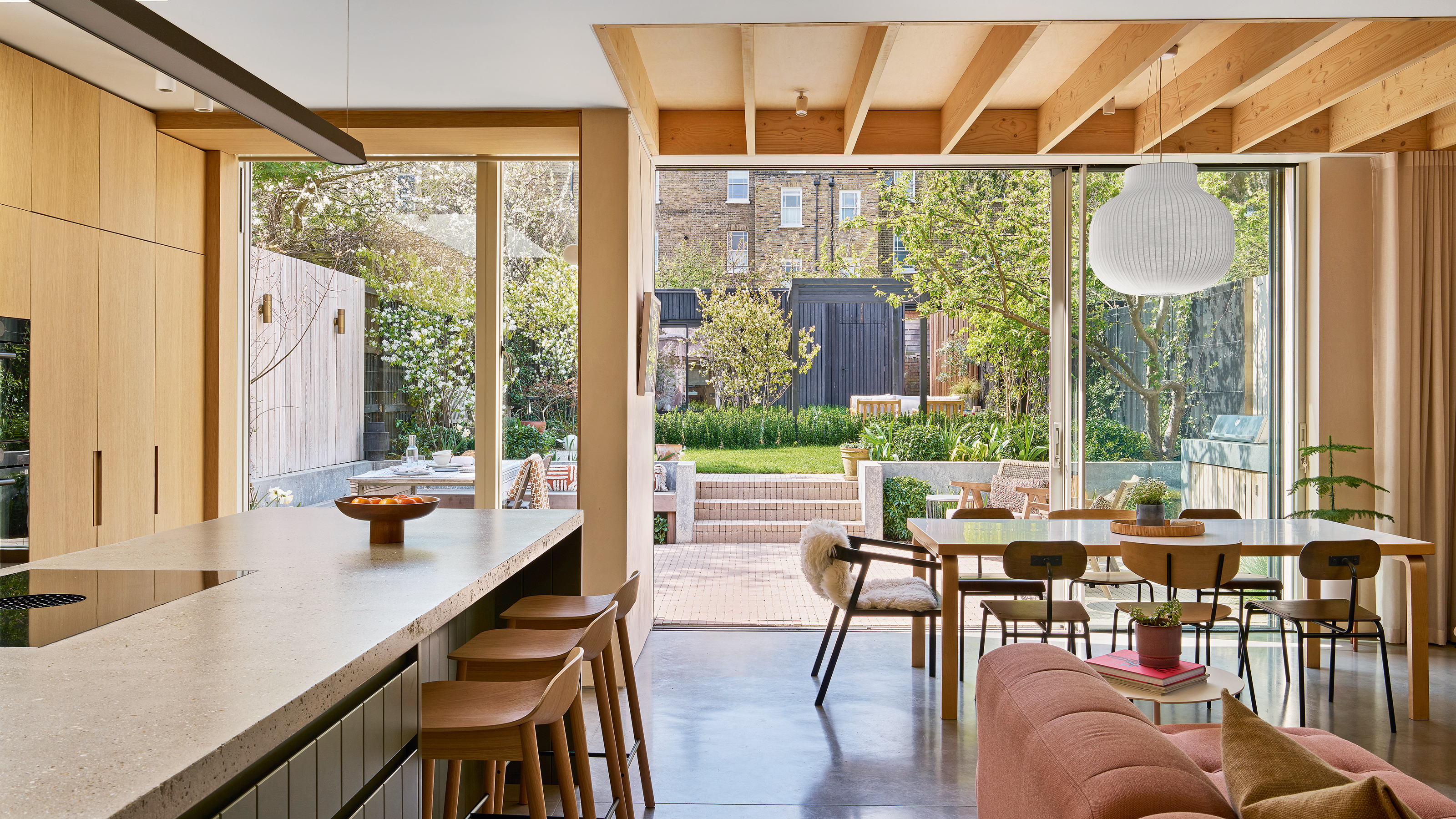 an open plan kitchen, dining and living area with slatted roof panels, a dusky pink sofa and a large kitchen island