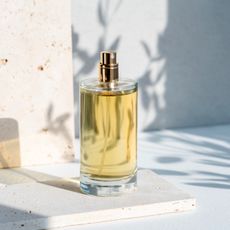 A perfume bottle on a white countertop with shadows of leaves behind it