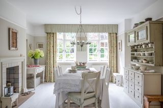 dining room with white painted floorboards and candle chandelier with vintage linen on table and bay window and old dressers