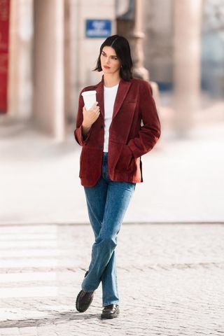 Kendall Jenner wears blue jeans, affordable loafers, red wine velvet jacket and a white tee as she carries a coffee cup