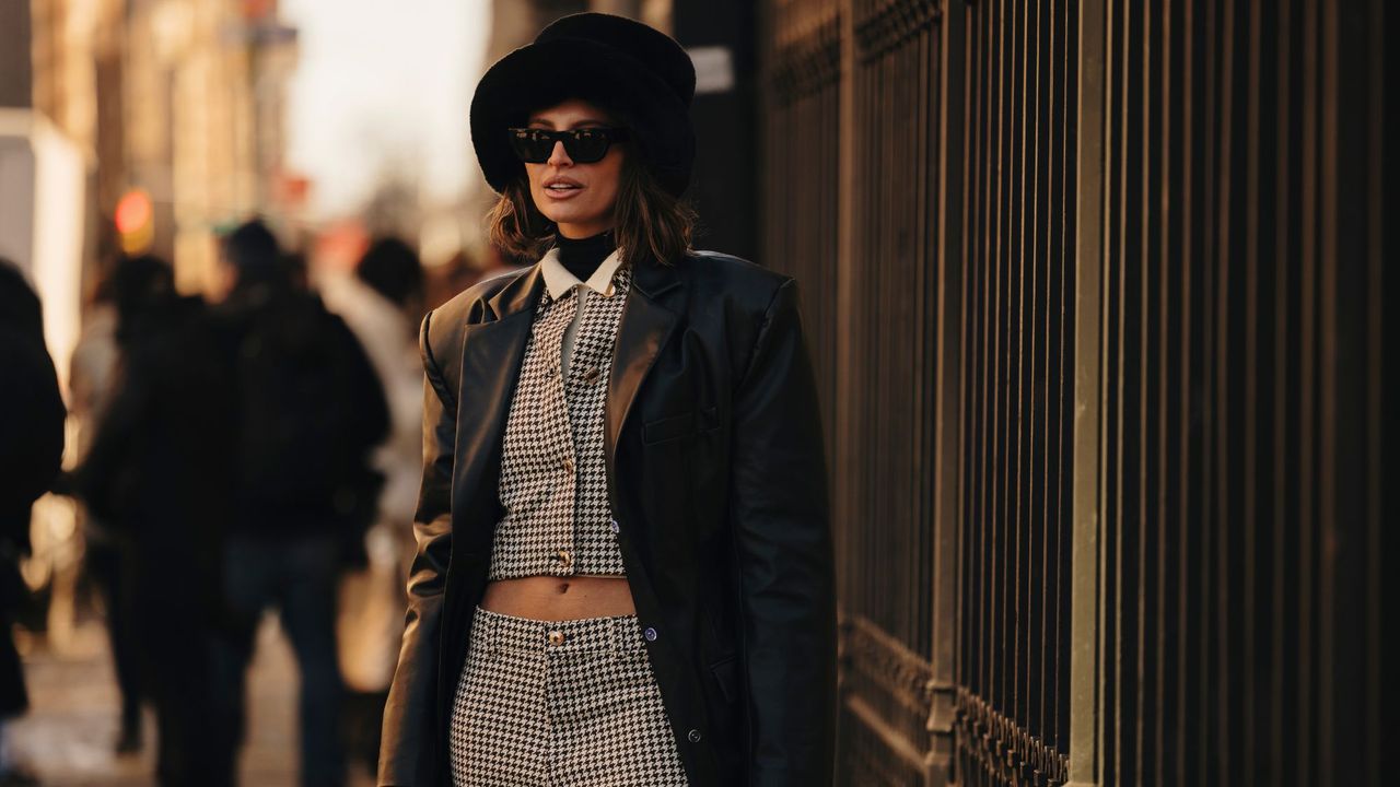 A guest at New York fashion week wearing a fur hat, houndstooth suit and leather coat, the perfect outfit for a smoky perfume