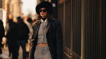 A guest at New York fashion week wearing a fur hat, houndstooth suit and leather coat, the perfect outfit for a smoky perfume