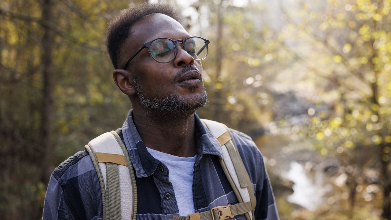 A man pauses during a hike to close his eyes and breathe. 