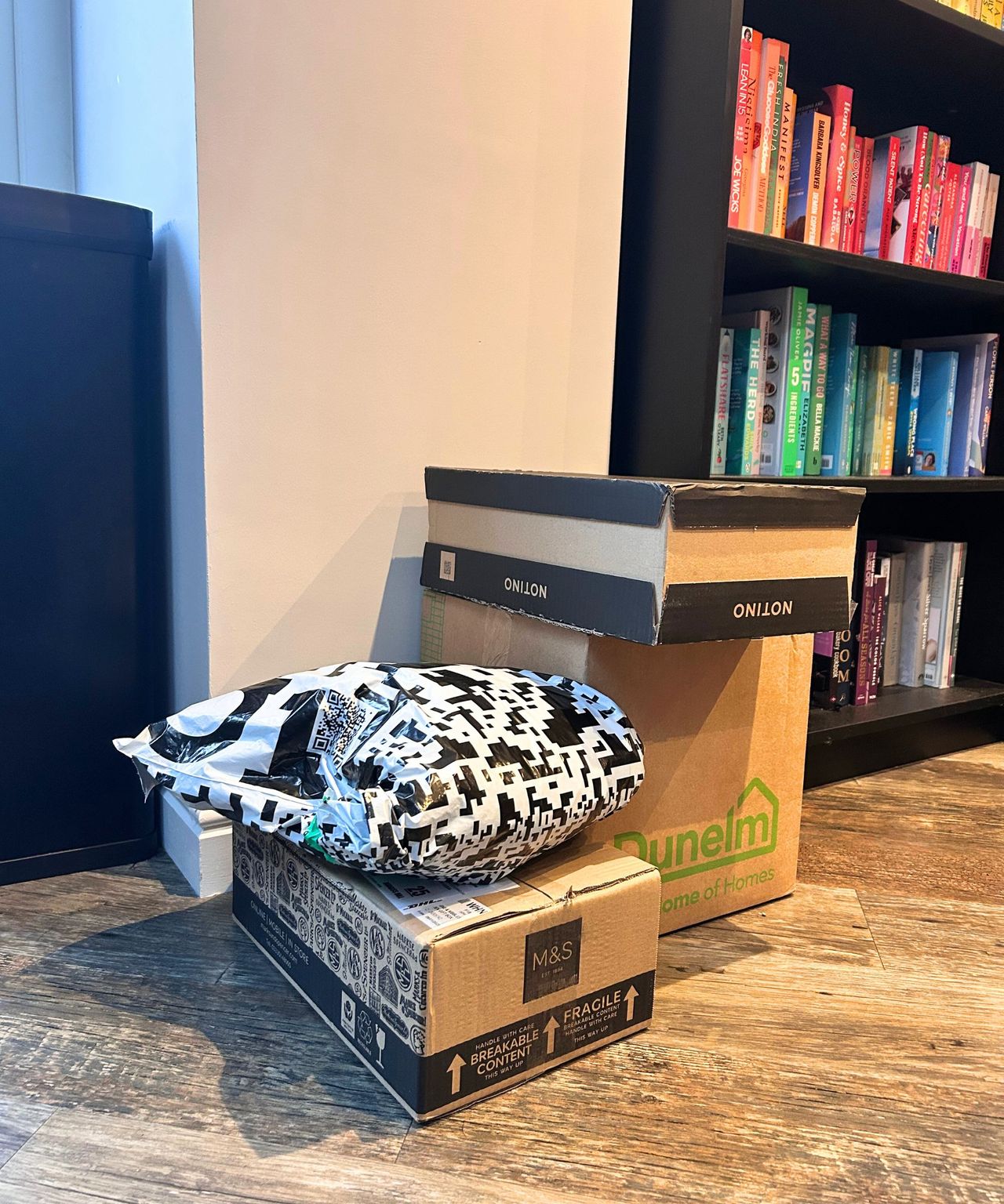 Stack of boxed items on the floor next to a colour-coordinated book shelf