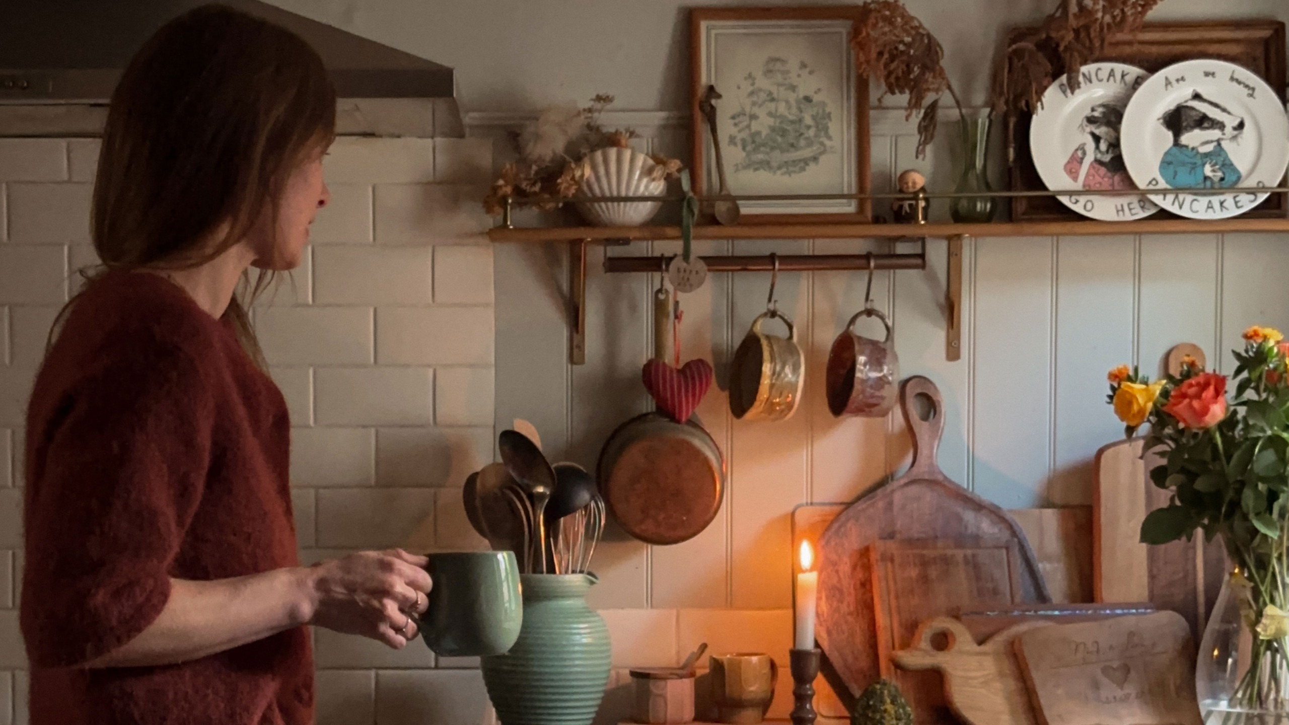 Woman holding mug in kitchen with candle burning