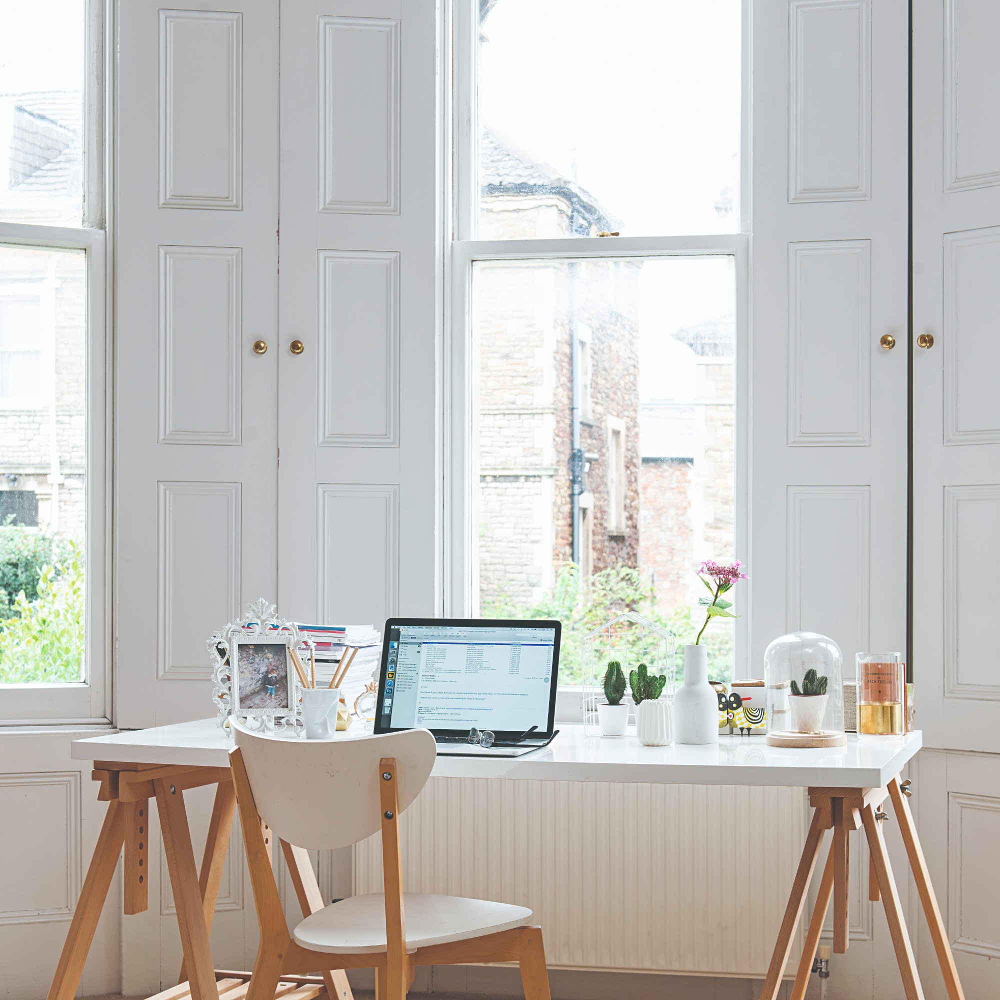A bay window with white shutters and a desk with a matching chair