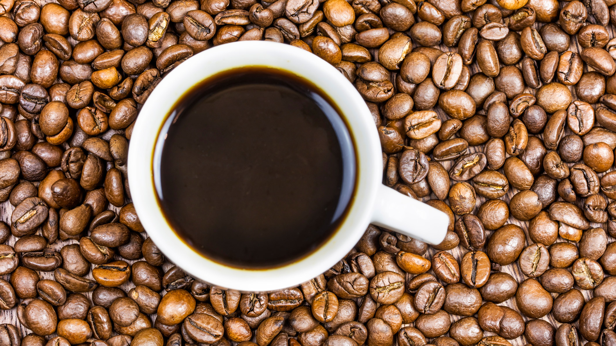 A cup of black coffee surrounded by coffee beans