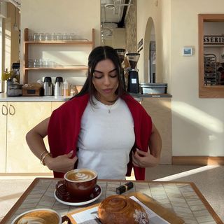 Woman looking down at a Chanel lipstick while adjusting her sweater at a coffee shop.