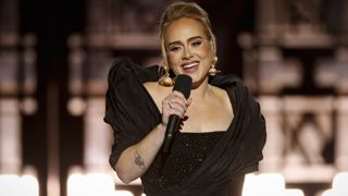Adele performs with a mic in her hand and a smile on her face