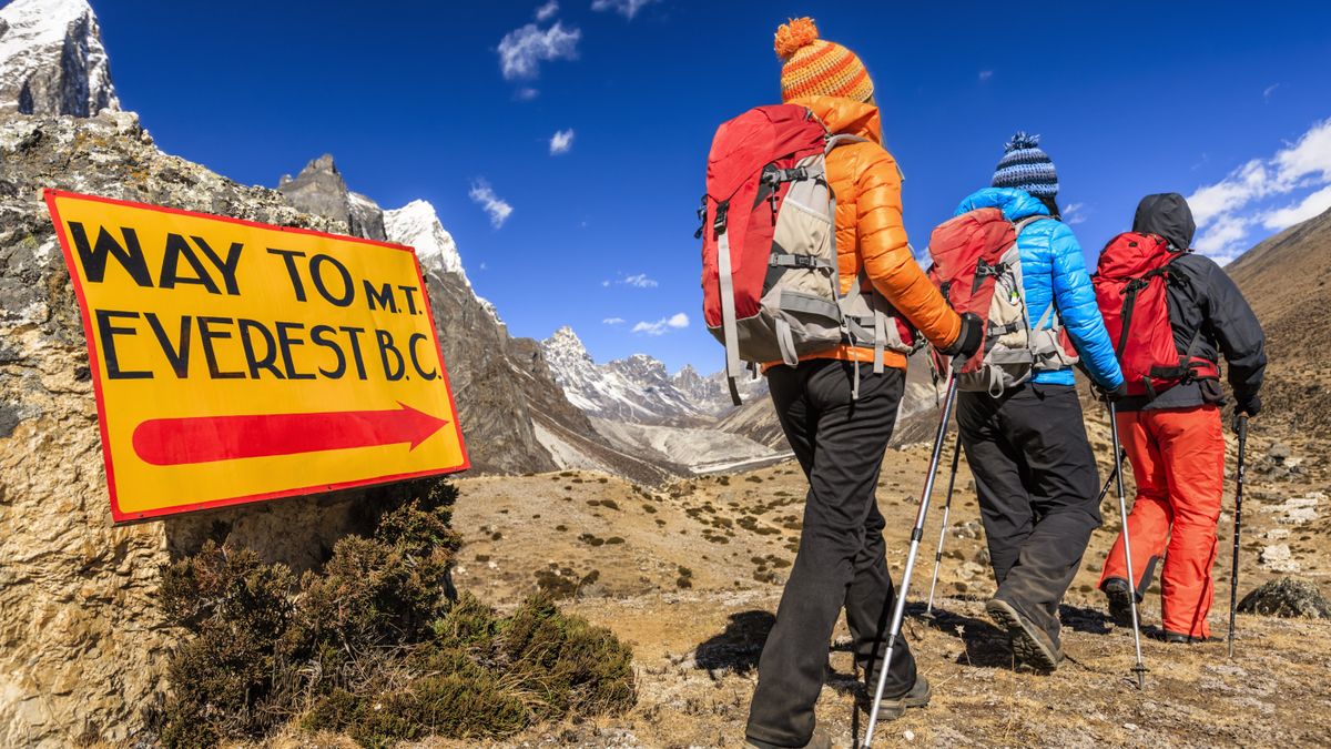 Three hikers passing a sign for Everest Base Camp