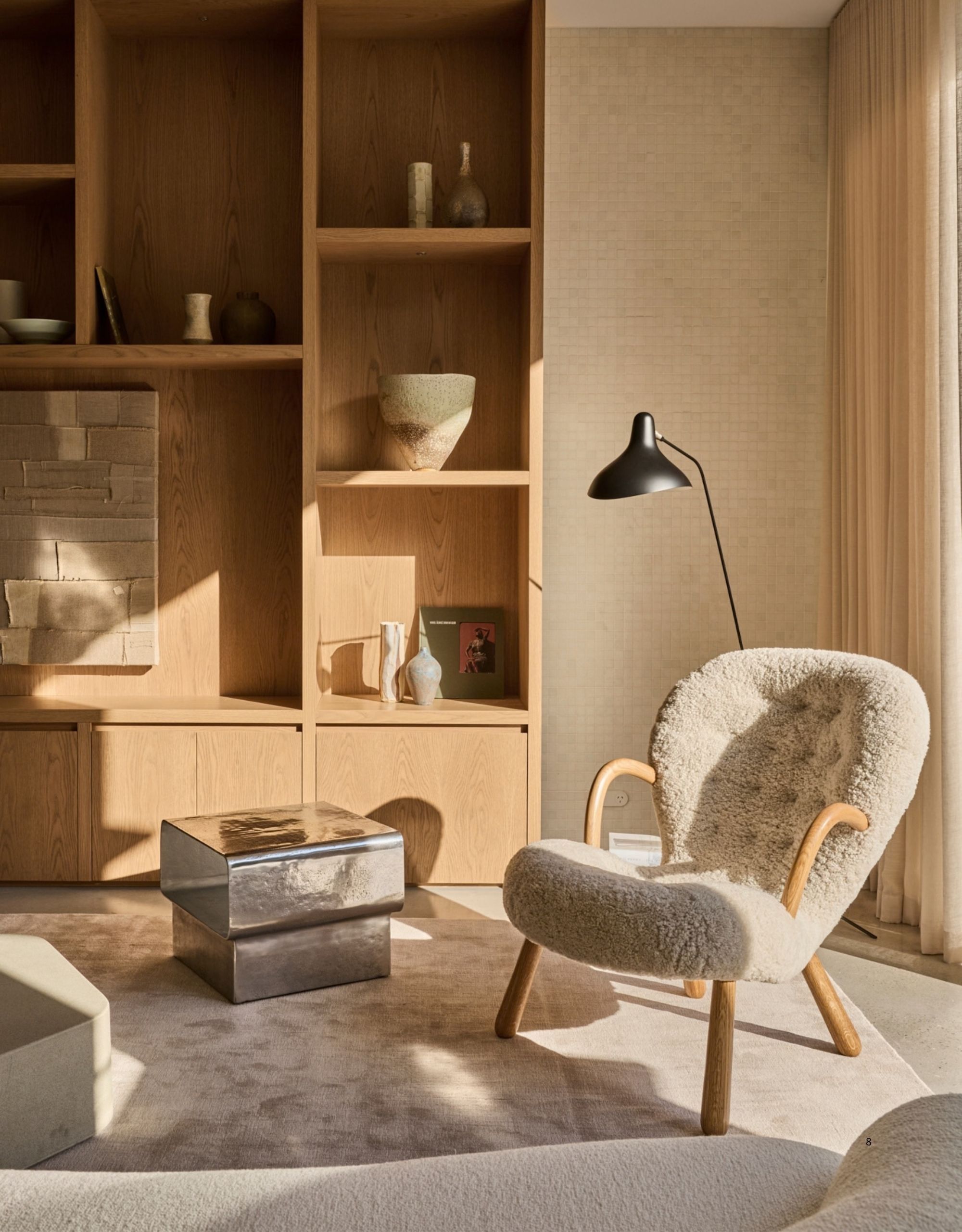 Image of a boucle side chair in a neutral living room with a modern build. There is a large wooden built-in with lot of decor on the shelves, a metal side table, a rug, and a white sofa.