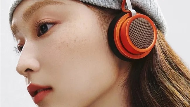 A woman wearing a pair of orange Edifier Doo Ace over-ear headphones.