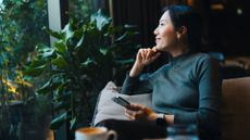 Woman smiling, holding phone and looking out of the window in a cafe, sitting on sofa after doing brain health exercises