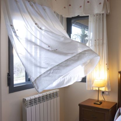 Open window in bedroom with sheet curtain billowing in the breeze