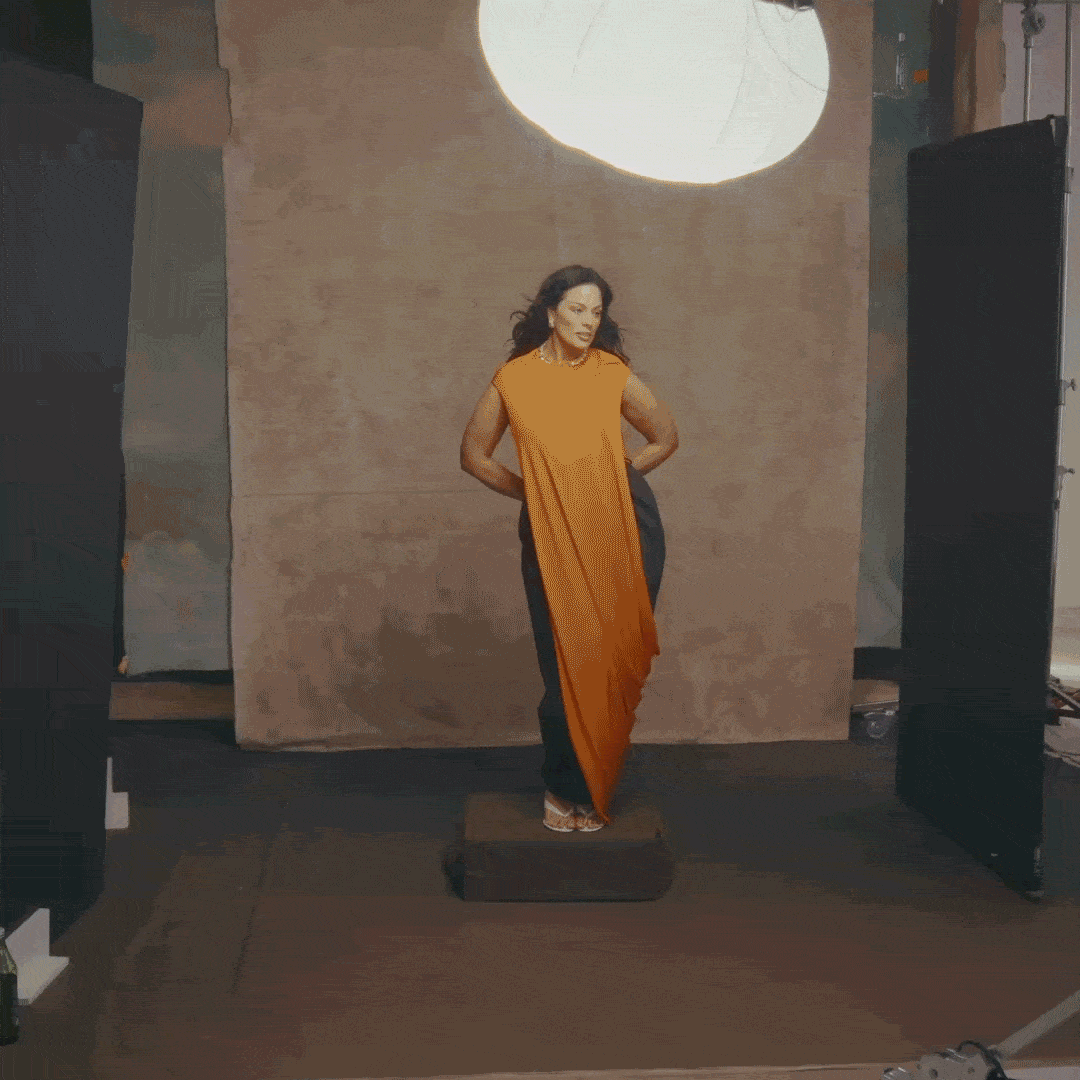 Ashley Graham in a gif with wind blowing her hair as she wears a long orange gown and poses on a photo set