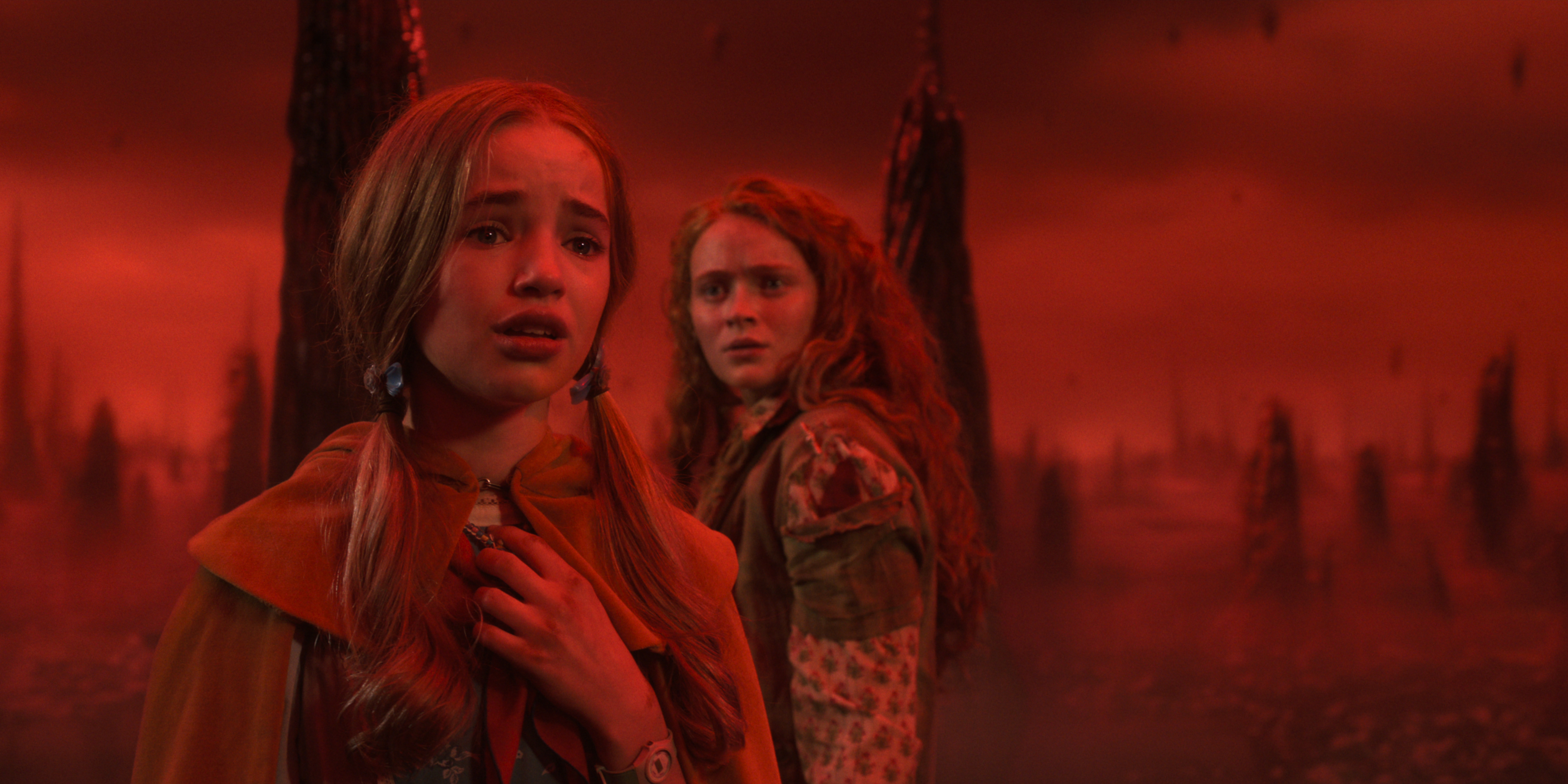 Nell Fisher as Holly Wheeler wearing her holly the hero cloak and Sadie Sink as Max Mayfield looking scared in a red lit upside down in Stranger Things: Season 5