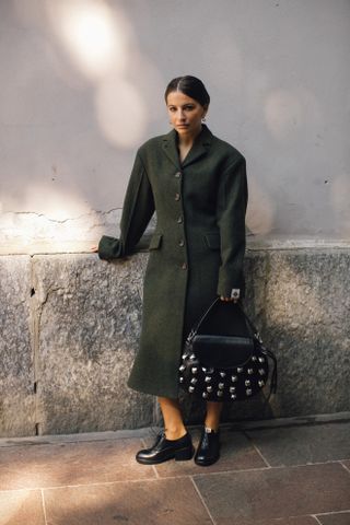 Woman in green coat and decorated bag.