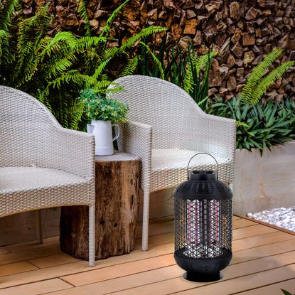 A small lantern electric patio heater on the flloor by two grey rattan outdoor chairs