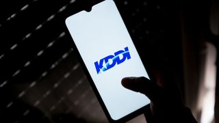 A KDDI logo seen displayed on a smartphone screen being held by a hand