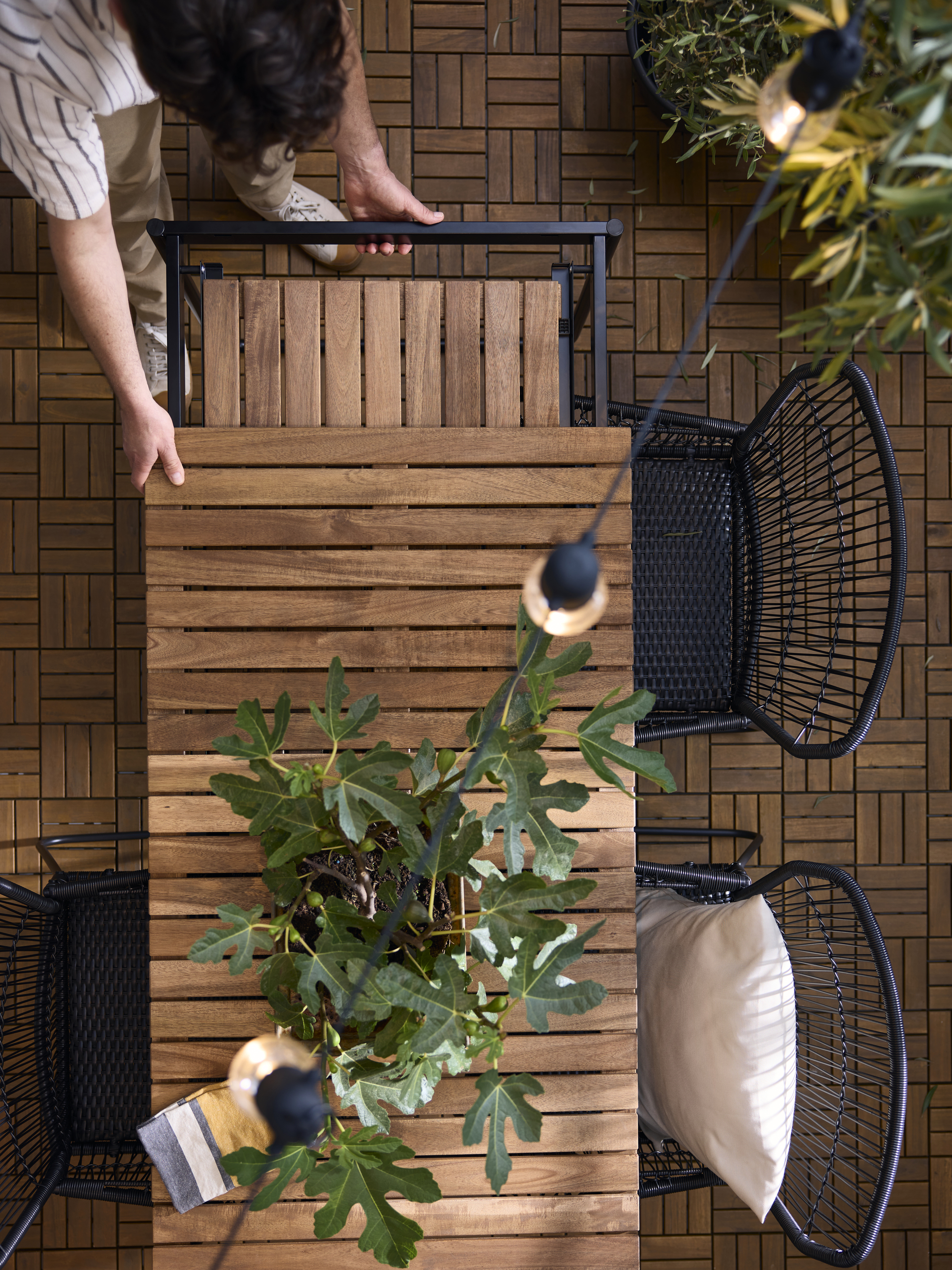 IKEA extendable table on an outdoor balcony with greenery, black dining chairs, string lights, and potted plants