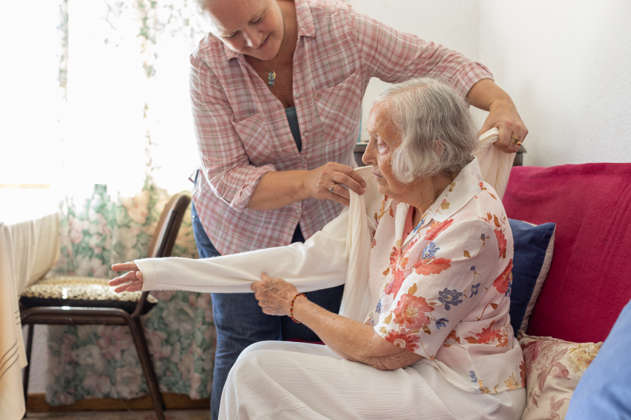 A middle aged female carer helping an older woman put her jumper on