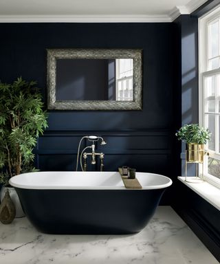 Black paneled bathroom with white woodwork and ceiling, marble floor tiles, plants