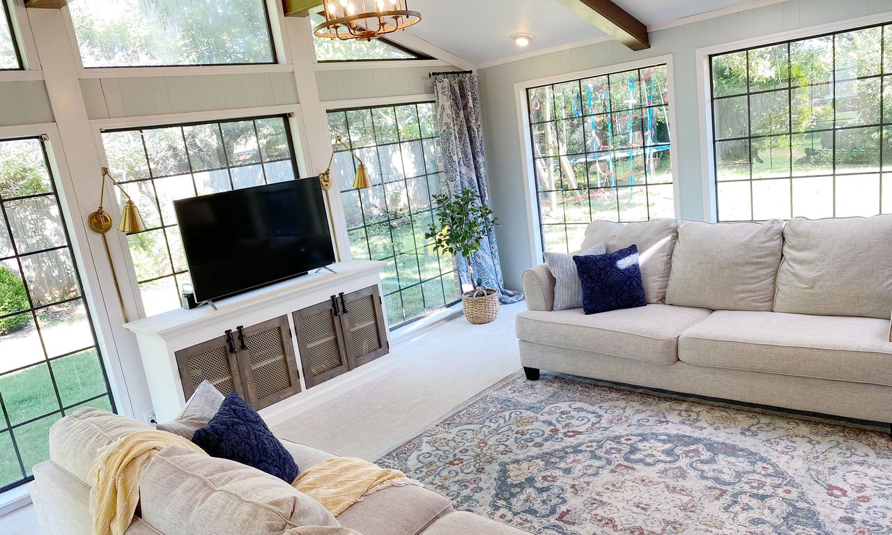 Light living room with crittal-style windows, blue patterned rug, cream fabric couch and wooden TV stand with black accents