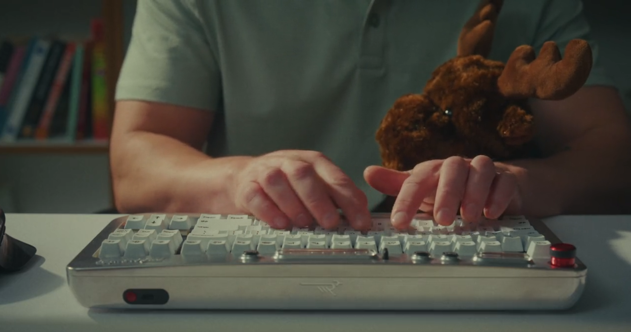 The Freewrite Wordrunner keyboard seen in operation on a desk.  We are looking at the back of the keyboard, directly at the typist. The typist has a fluffy reindeer toy tucked into their arm as they type.