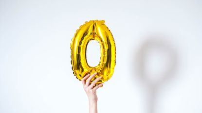 Orgasm questions: A woman holds up an inflatable golden balloon in the shape of the letter O