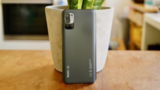 A Xiaomi Redmi Note 10 5G from the back, resting against a plant pot