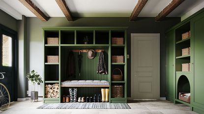 Large green boot room with painted green walls, bespoke wall shelving painted green with storage baskets, hooks, seating, stone flooring with rug, white painted door, white painted ceiling with wooden beams